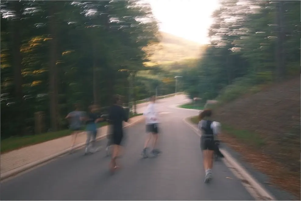SOURR-Läufer:innen auf einer sonnigen Straße durch den Wald, in Bewegungsunschärfe